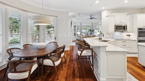 A spacious kitchen with white cabinetry, a wooden dining table, and a large island with a sink.