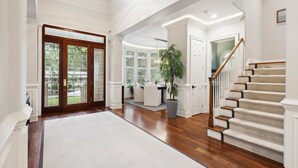 A spacious foyer with a grand staircase, a large wooden door, and a potted plant.