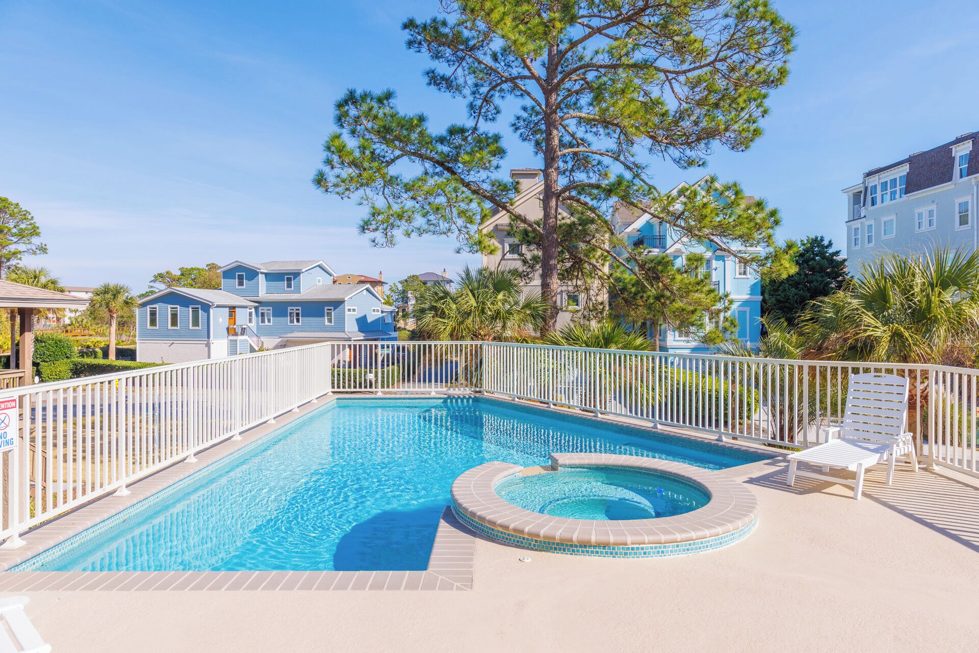 A swimming pool with a hot tub, surrounded by a white fence, and a tree in the center.