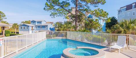 A swimming pool with a hot tub, surrounded by a white fence, and a tree in the center.