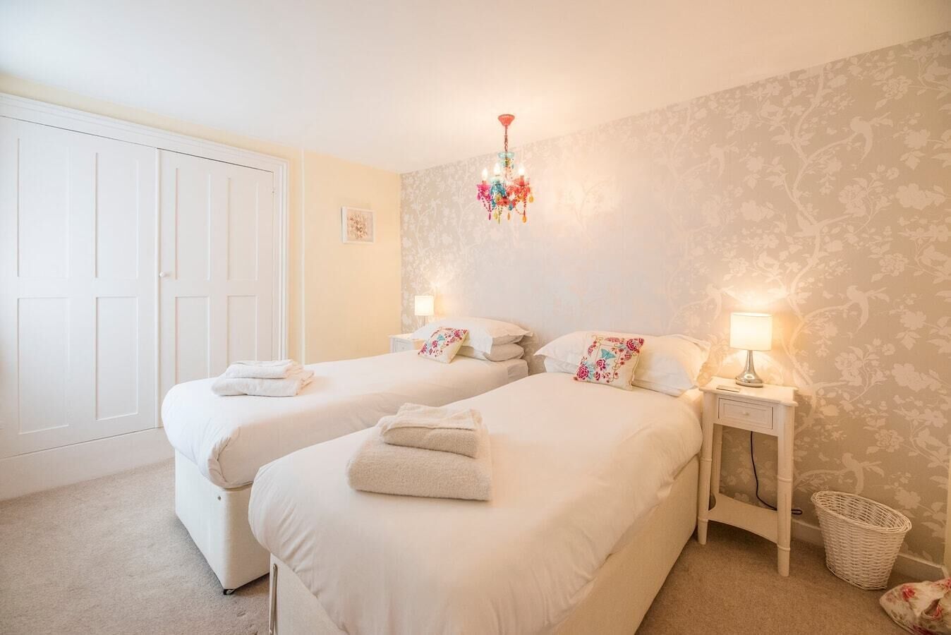 A bedroom with two beds, a chandelier, a nightstand with a lamp, and a door.