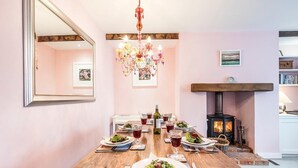 Un coin repas avec une table en bois dressée pour le repas, un lustre, une cheminée et un miroir au mur.