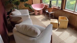 Una habitación acogedora con un ventanal grande, un sillón rosa, un sofá blanco y una planta en maceta.