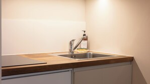 Una cocina con un lavamanos de acero inoxidable, una encimera de madera y una botella de detergente.