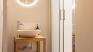 Un baño con tocador de madera, lavabo sobre encimera, dispensador de jabón y cabina de ducha de vidrio.