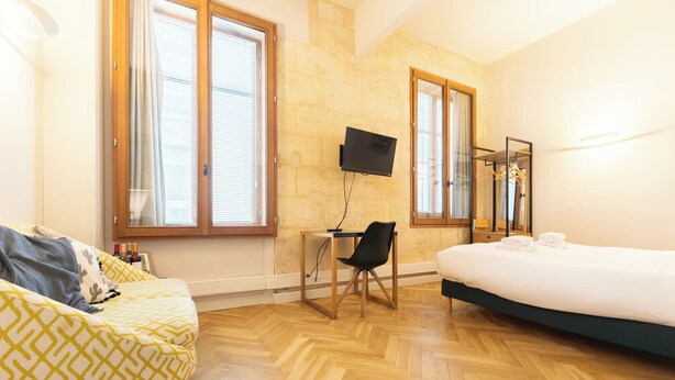 Habitación de hotel con cama, escritorio con silla, televisión y ventana grande.
