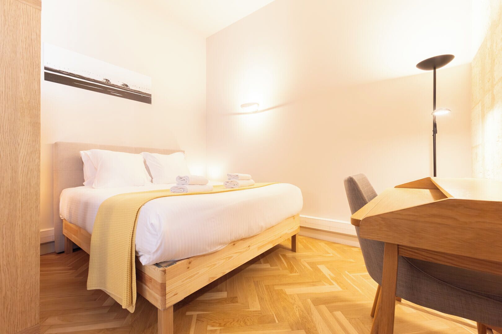 Habitación de hotel con cama, mesita de noche, lámpara y suelo de madera.