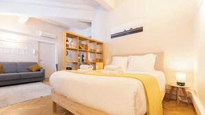 A hotel room with a bed, a sofa, a wooden cabinet with wine bottles, and a painting on the wall. - Superb Bordeaux flat in hypercentre for *4 people* (Bordeaux)