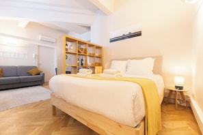 Une chambre dâhĂŽtel avec un lit, un canapĂ©, une armoire en bois contenant des bouteilles de vin et un tableau au mur.