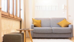A living room with a grey sofa, two mustard pillows, a small wooden side table, and a grey ottoman. - Superb Bordeaux flat in hypercentre for *4 people* (Bordeaux)