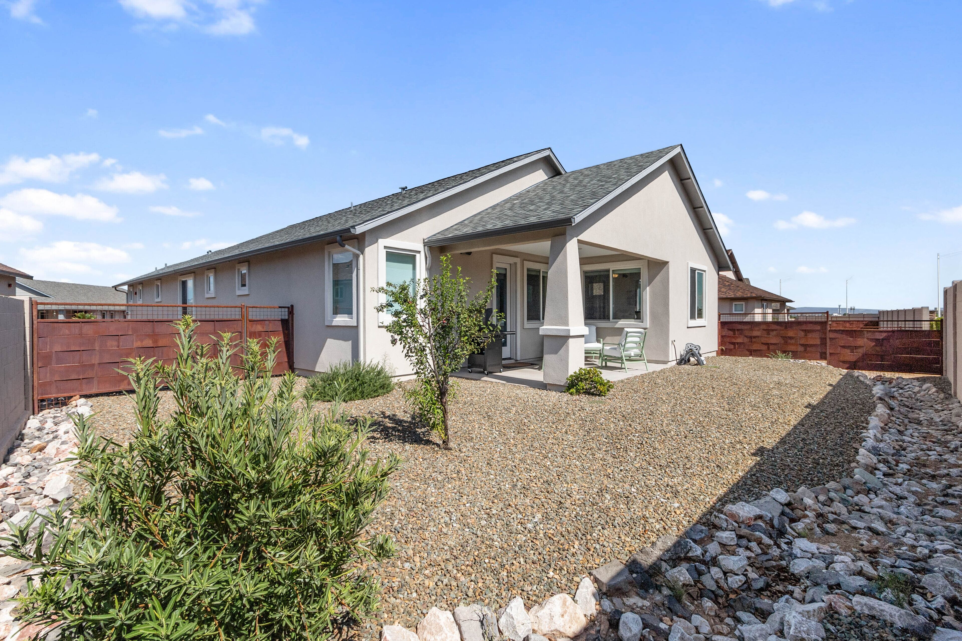 A modern house with a covered patio, a gravel driveway, and a small garden with shrubs.