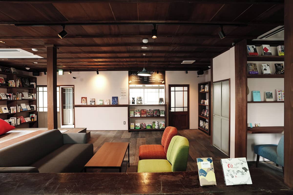Ein gemütliches Interieur mit Holzbalkendecke, einer Couch, einem farbenfrohen Sessel und Bücherregalen voller Bücher.
