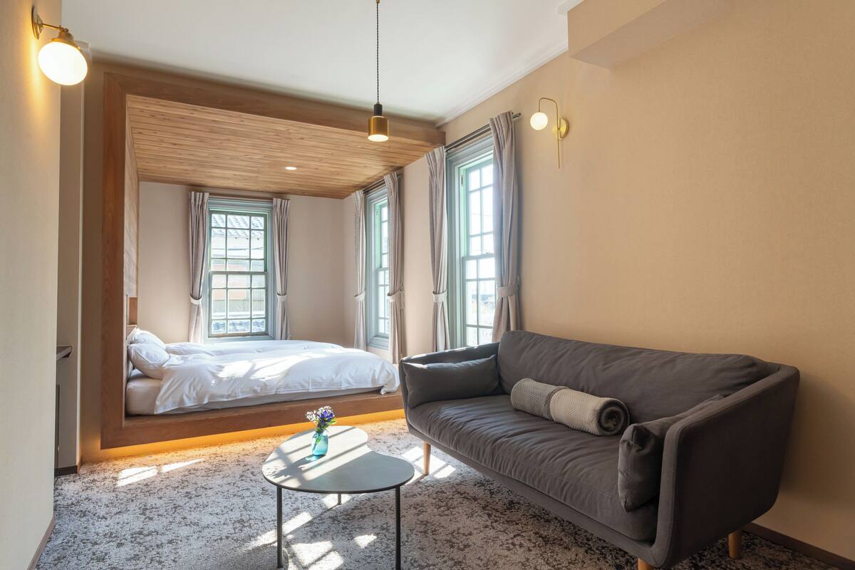 Ein Schlafzimmer mit einem Bett, einem Schlafsofa, einem kleinen Tisch und einem Fenster mit Vorhängen.