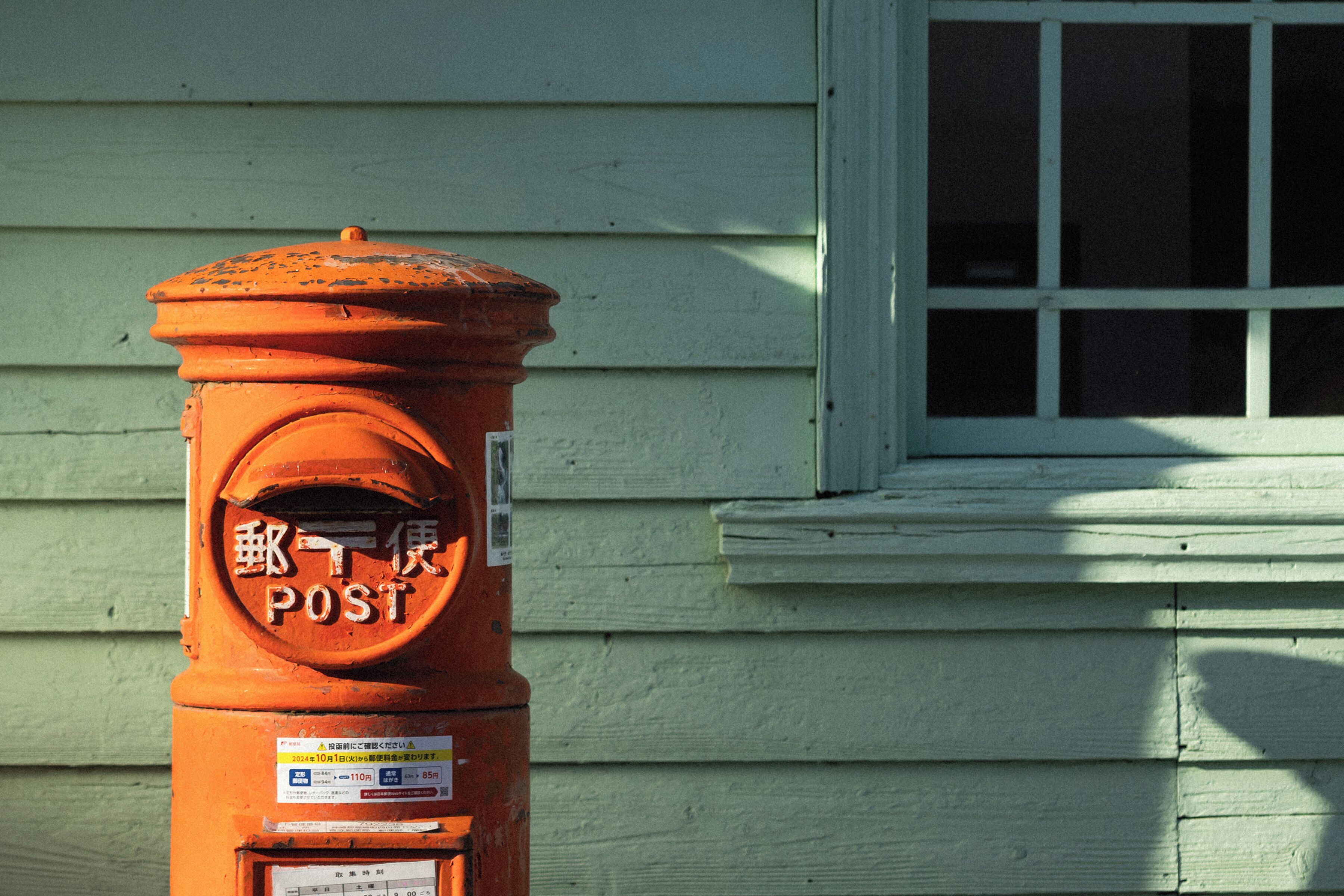 An orange fire hydrant with a sign that reads "POST" and some text in another language.