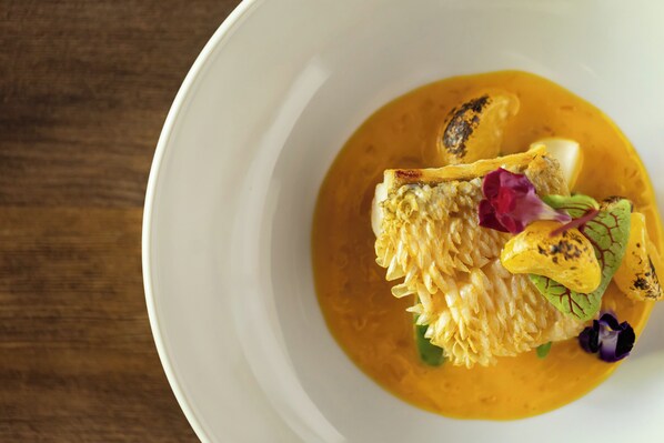 A white bowl with a yellow sauce, a piece of fish, and some vegetables.