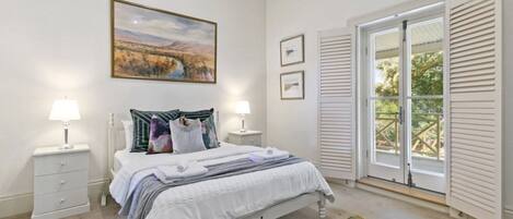 A bedroom with a bed, two bedside tables with lamps, a large window with shutters, and a painting above the bed.
