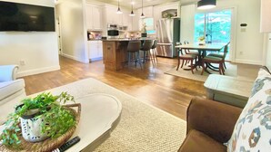 Une cuisine moderne avec des meubles blancs, un îlot central, des tabourets de bar et un coin repas comprenant une table et des chaises.
