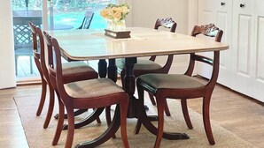 Un espace repas comprenant une grande table, six chaises, un lustre et une vue sur un jardin, visible à travers des portes vitrées.
