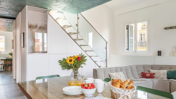 A modern kitchen with a marble countertop, a dining area with a glass table, and a staircase leading to another level. - Penthouse Massena - 2 bedroom apartment (Nice)