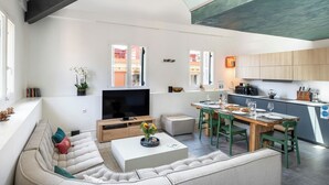Een moderne woonkamer met een grote televisie, een bank, een eethoek en een keuken.