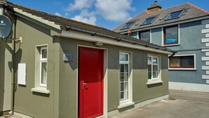 A single-story building with a red door, white-framed windows, and a satellite dish on the left. - Beachfront Break - 2 bedroom home (County Kerry)