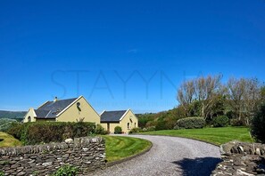 A two-story house with a stone wall entrance, a gravel driveway, and a well-maintained lawn. - Waterfront Annex one bedroom annex (Dingle)