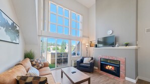 A living room with a sofa, a coffee table, a fireplace, a TV, and large windows.
