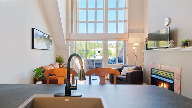 A modern kitchen with a large window, a fireplace, and a dining area with two sofas.