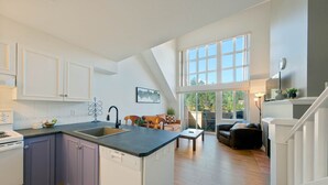 A modern kitchen with a central island, a dining area with a sofa and table, and a staircase leading to a lofted space.