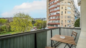 En balkon med et træbord og stole, med udsigt over et bybillede med bygninger og træer.