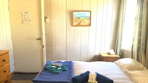 A hotel room with a bed, a wooden dresser, a painting on the wall, and a window with curtains.
