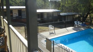 A swimming pool with a fenced deck, surrounded by a building with a flat roof and a covered patio area.
