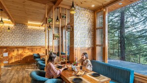 A cozy wooden interior with a dining area, blue upholstered seating, and geometric patterned walls. - Zostel Kotgarh (Narkanda) (Kumharsain)