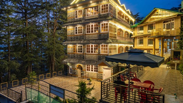 A multi-story hotel with a prominent sign, outdoor seating area, and a staircase leading to the entrance. - Zostel Kotgarh (Narkanda) (Kumharsain)