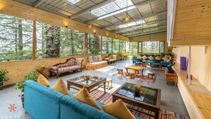 A spacious, well-lit room with large windows, wooden furniture, and a variety of seating options. - Zostel Kotgarh (Narkanda) (Kumharsain)