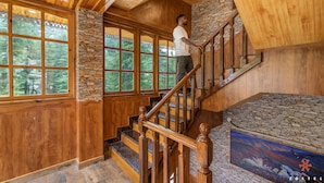 A wooden staircase with stone accents and a view of the outdoors through large windows. - Zostel Kotgarh (Narkanda) (Kumharsain)