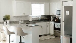 Une cuisine moderne avec des meubles blancs, un îlot central doté de tabourets, un four encastré et un réfrigérateur en acier inoxydable.
