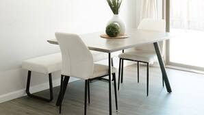 Un coin repas avec une table ronde, des chaises blanches, un vase avec des plantes et un tableau au mur.