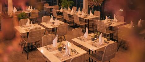 Un comedor interior con mesas dispuestas para el servicio, iluminación ambiental y un centro de mesa con planta decorativa.