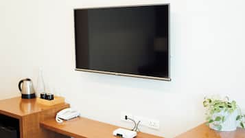 Habitación de hotel con televisor de pantalla plana montado en la pared, un escritorio de madera con teléfono, cafetera y regleta de enchufes.