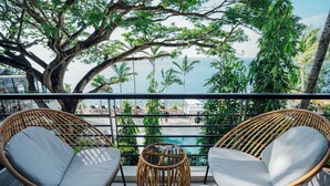 A balcony with wicker chairs and a small table, overlooking a pool and palm trees. - Solitude Acacia Resort (Mabini)