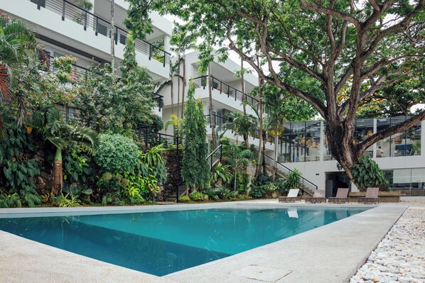 A swimming pool surrounded by lush greenery and a modern building with balconies.