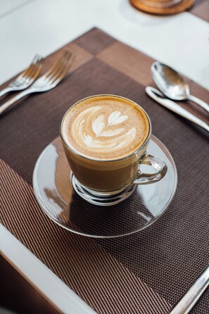 A cup of coffee with latte art on a saucer, placed on a placemat with cutlery.