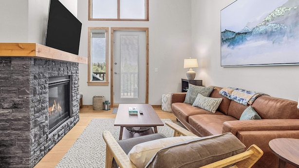 A living room with a fireplace, a sofa, a coffee table, and a painting on the wall. - Spring Creek Vacations 1 Bedroom Elevated Condo 405TM (Canmore)