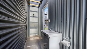 A compact, industrial-style bathroom with a stainless steel sink, a toilet, and a shower area.
