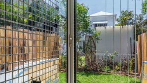 Ein modernes Badezimmer mit einer gläsernen Dusche, einer schwarzen Eckbadewanne und Blick auf Garten und Gebäude.
