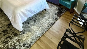Quarto moderno com uma cama grande, um ventilador de teto, uma cadeira azul e vista para o exterior pelas janelas.