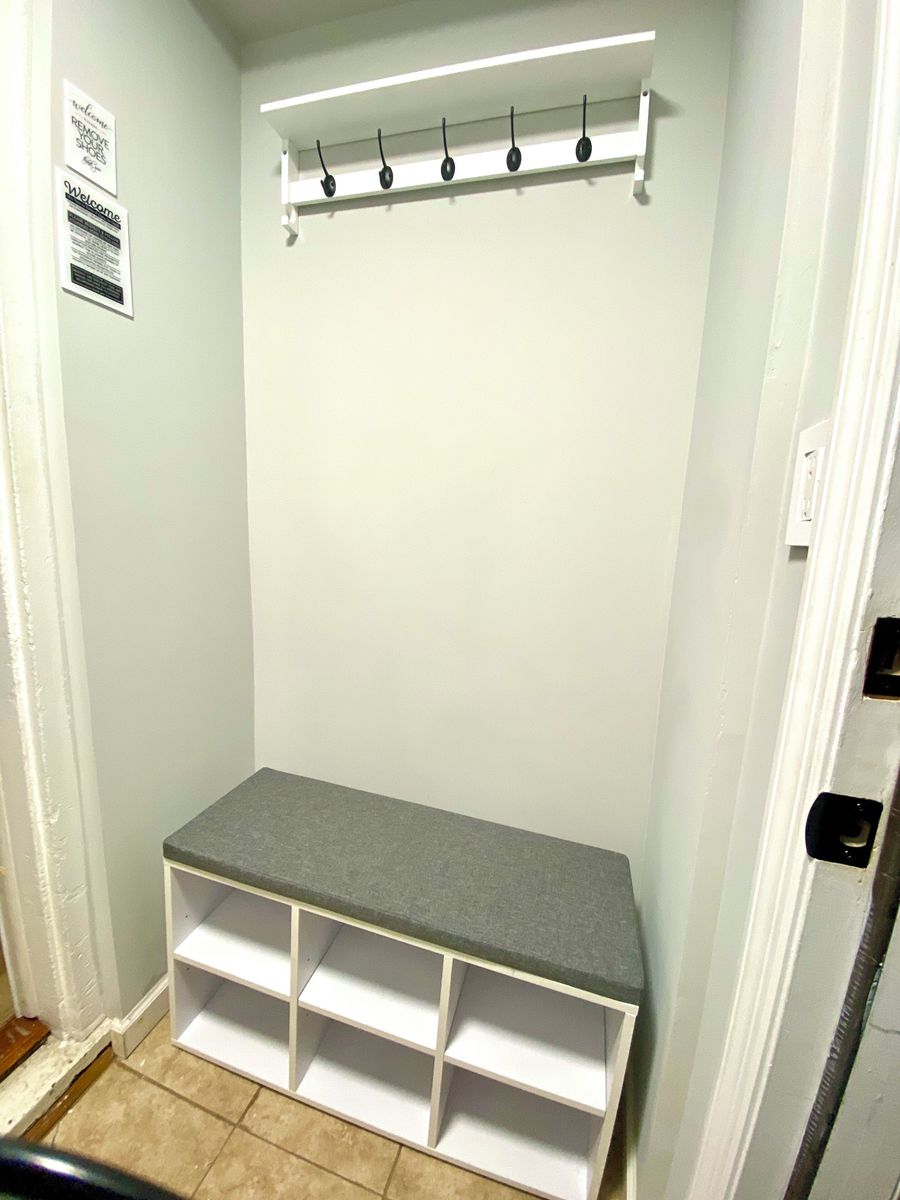 A small, white closet with a grey shelf and multiple white shelves below.