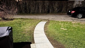 Uma trilha pavimentada serpenteia por uma área gramada, com um carro estacionado ao fundo.