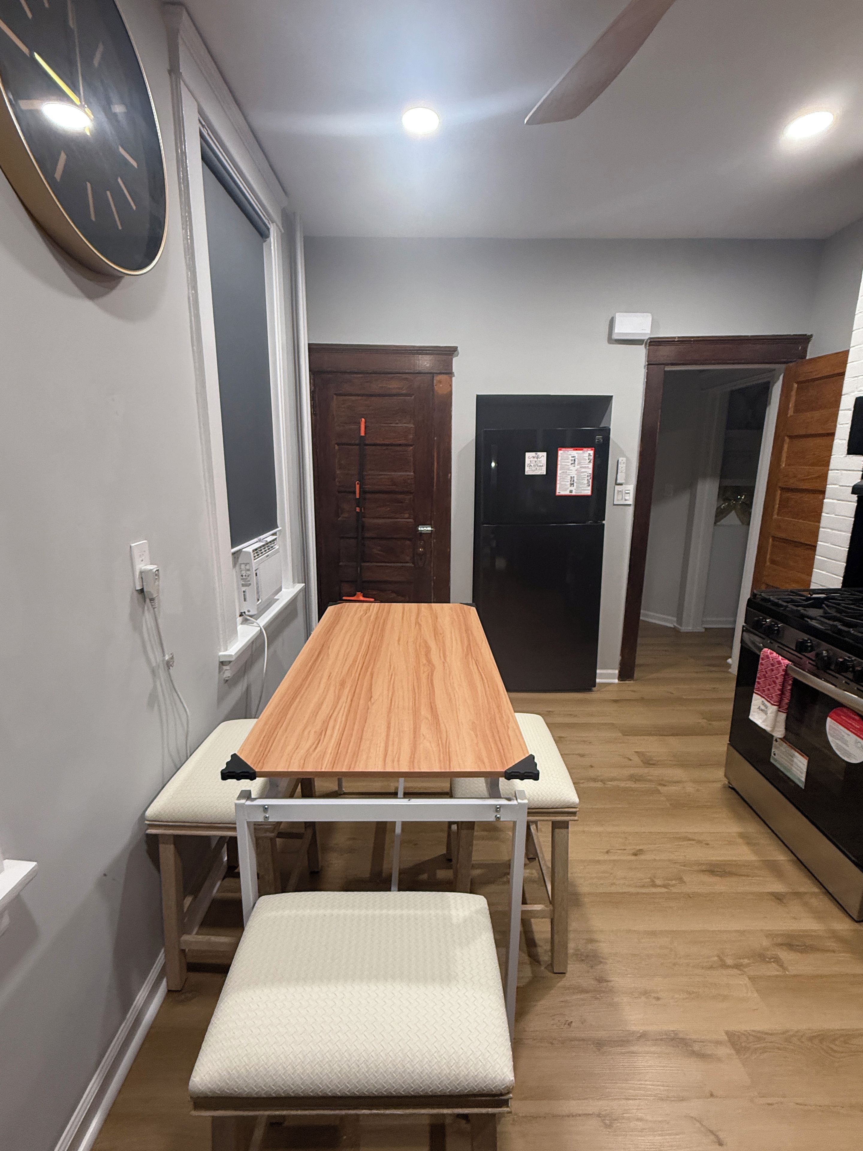 Una habitación con una mesa de madera, un banco y un refrigerador negro.